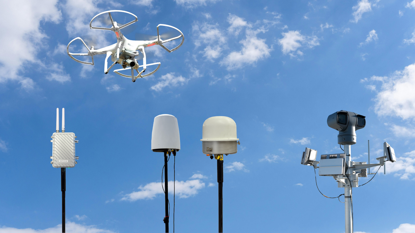 The multi-sensor drone-detection hardware: RF detection unit, Remote ID and radar domes, and a pan-tilt-zoom camera, watching for a drone overhead