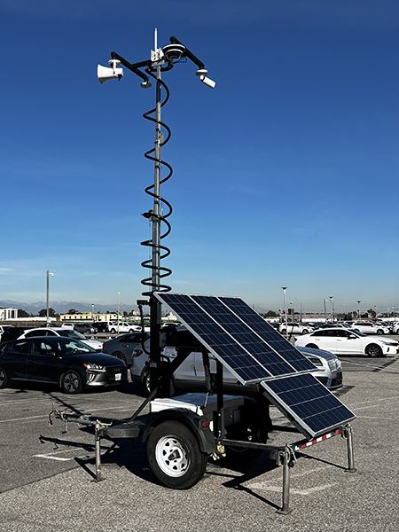Solar surveillance trailer with telescoping mast, cameras, and speaker in a parking lot